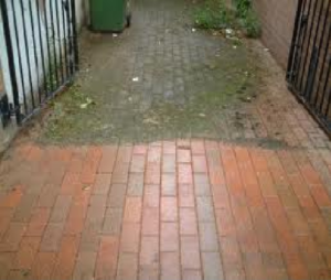 A brick walkway with a gate and trash can.